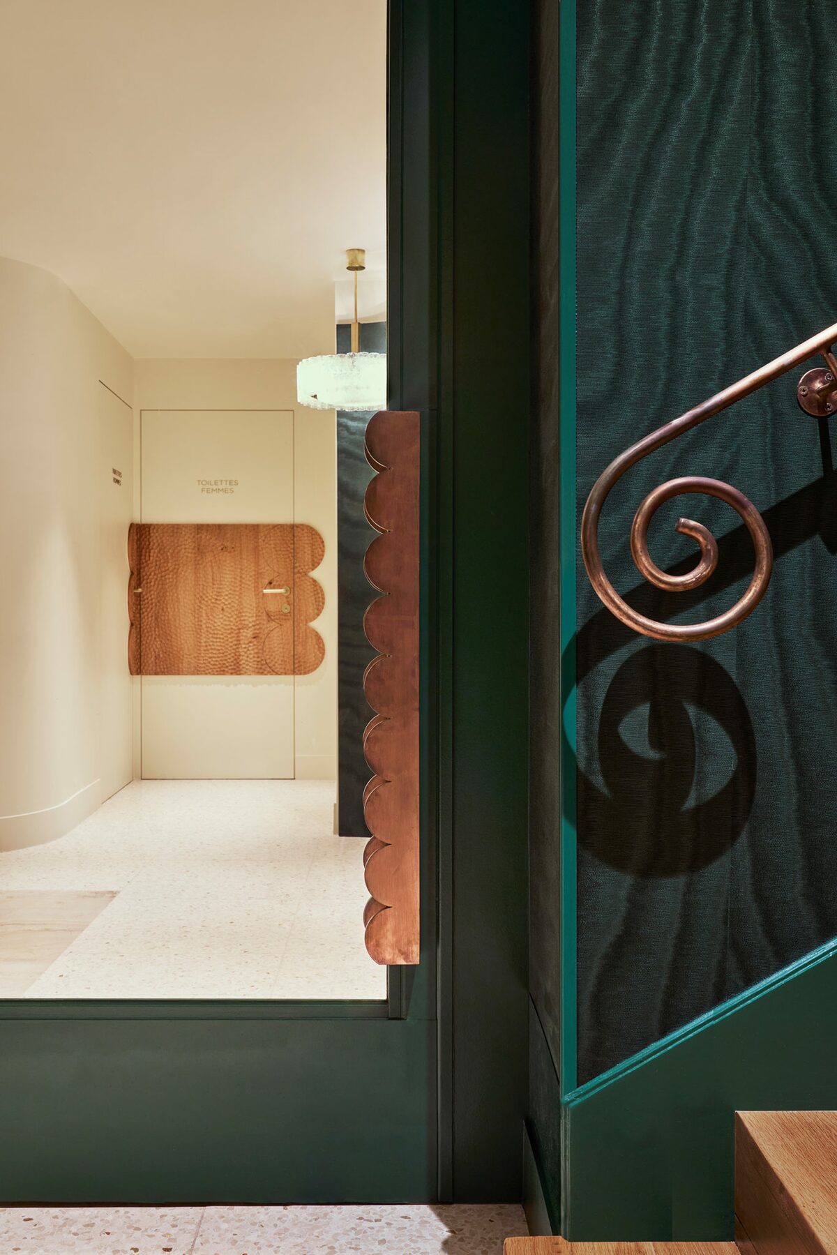 Porte en bois sculptée, escalier en bois avec papier peint moiré bleu nuit et rambarde en métal spirale - Projet Hôtel Spa Montalembert réalisé par Batiik Studio
