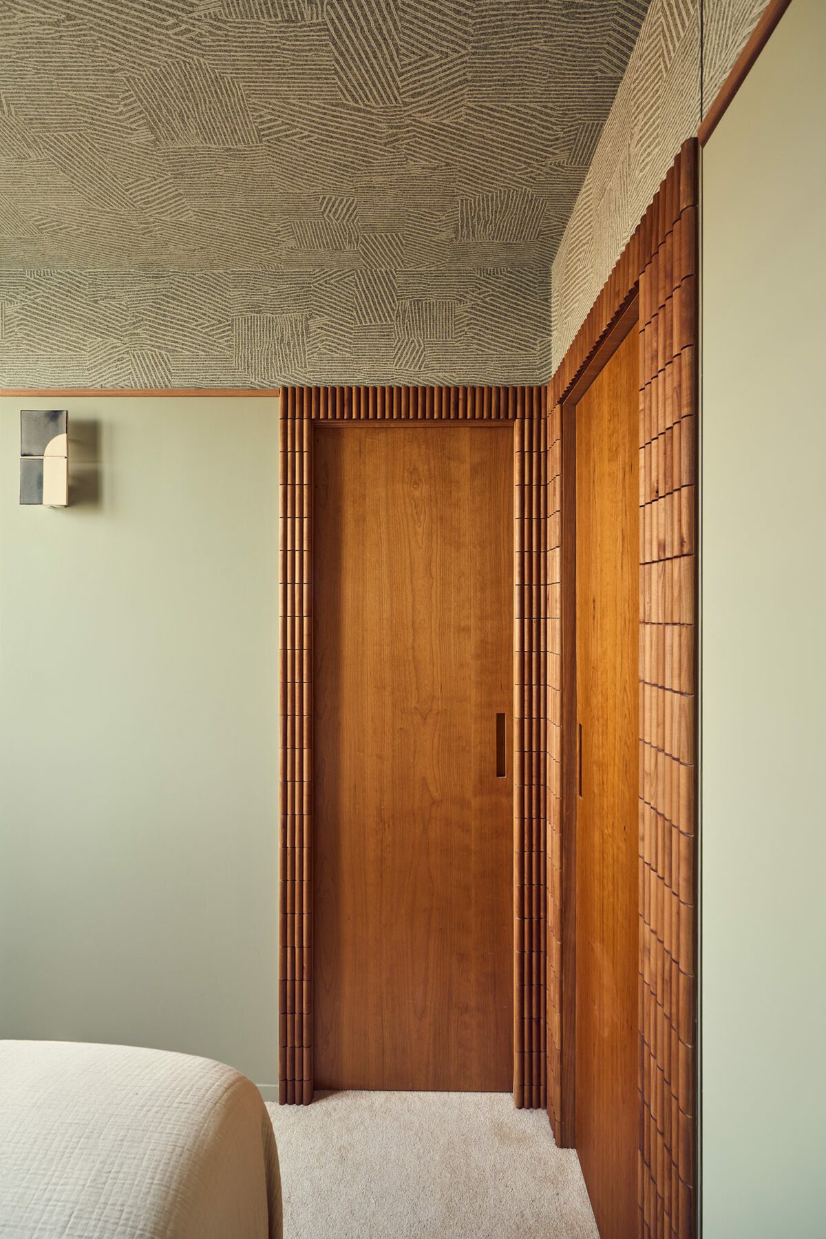 Plafond avec papier peint à motif, murs vert d'eau et porte en bois avec encadrements en relief bois. Projet Saint-Gervais à Paris réalisé par Batiik Studio.