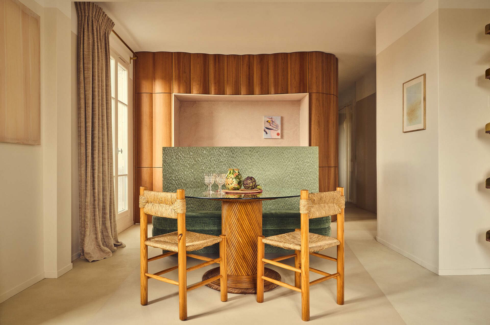 Appartement parisien. Sol en résine, chaise en rotin, table de salle à manger avec plateau en verre. Banquette en tissu vert. Cuisine en bois. Projet Saint-Gervais réalisé par Batiik Studio.