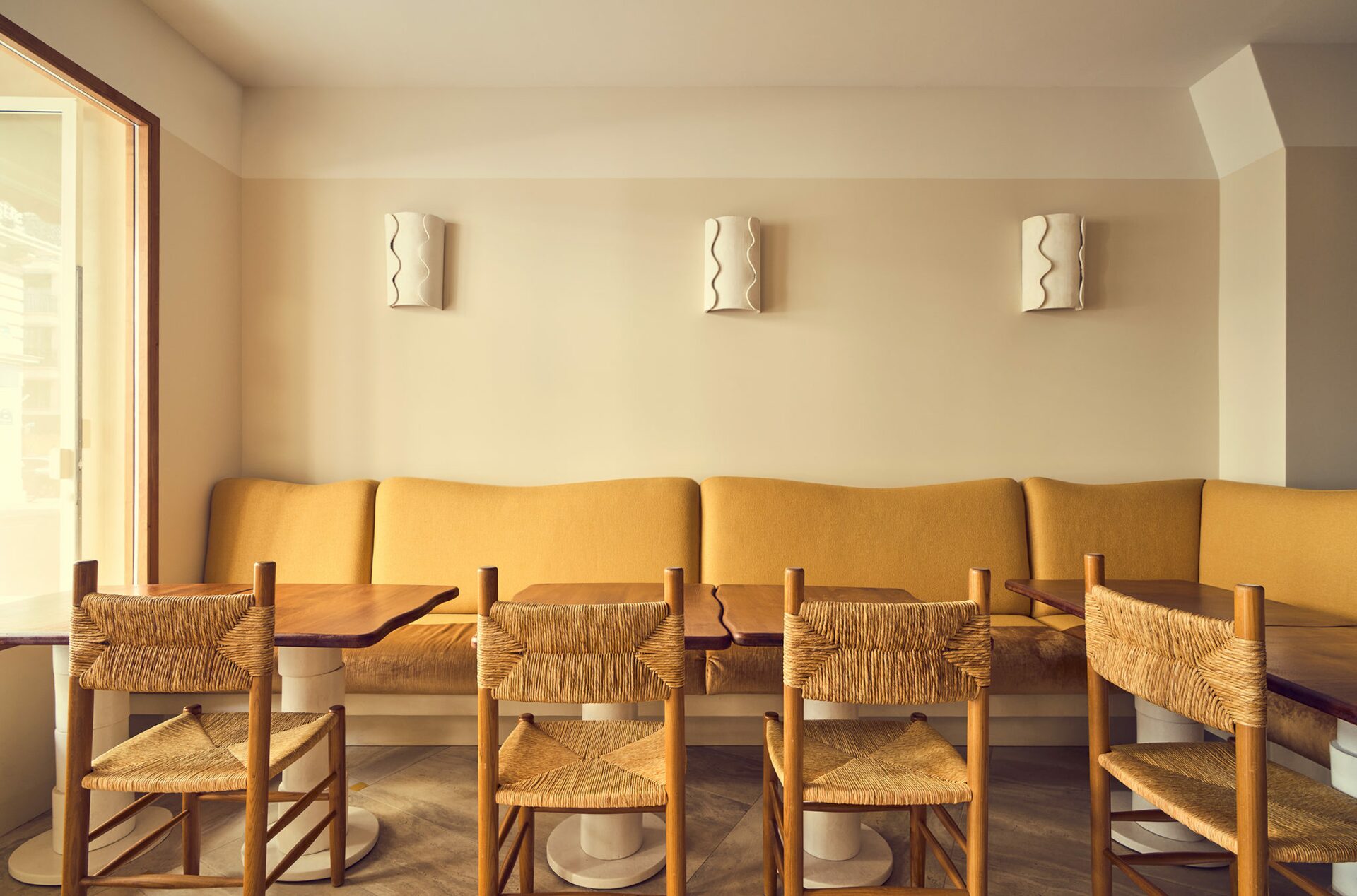 Banquette en velours jaune et tablette en bois. Chaise en bois et en rotin. applique blanche. Projet Love à Paris réalisé par Batiik Studio.