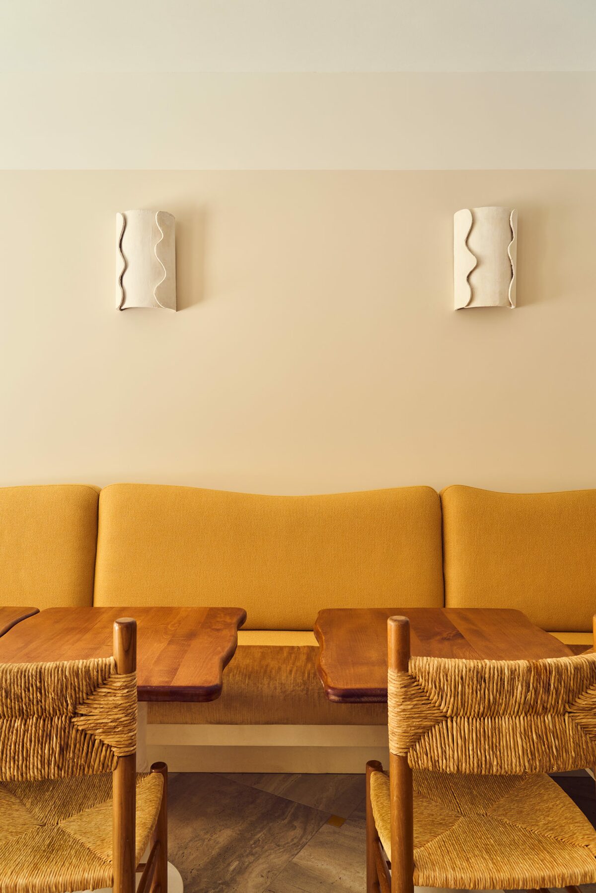 Banquette en velours jaune et tablette en bois. Chaise en bois et en rotin. applique blanche. Projet Love à Paris réalisé par Batiik Studio.