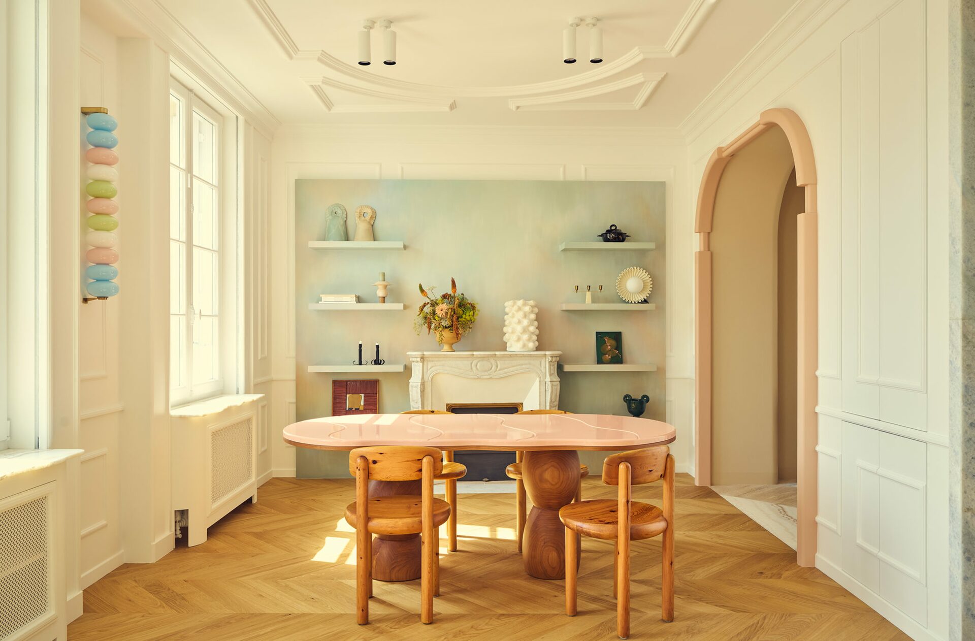Salle à manger dans appartement haussmannien avec table à manger ovale et chaises en bois. Parquet à chevrons, moulures et mur pastel. Projet Joséphine à Paris signé Batiik Studio.