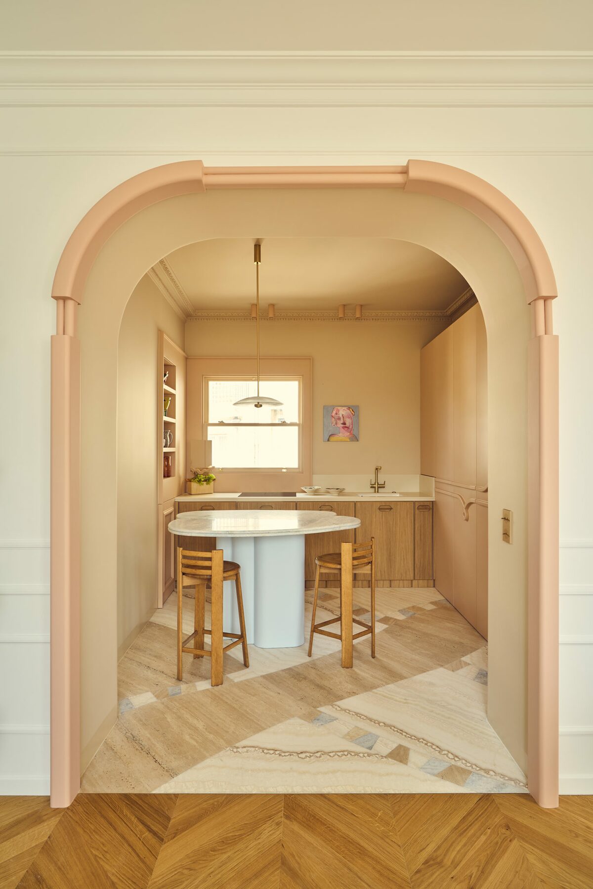 Cuisine haussmannienne avec rangements muraux beiges rosés. Carrelage et parquet. Chaises haute en bois, ilot central. Projet résidentiel Joséphine à Paris réalisé par Batiik Studio.