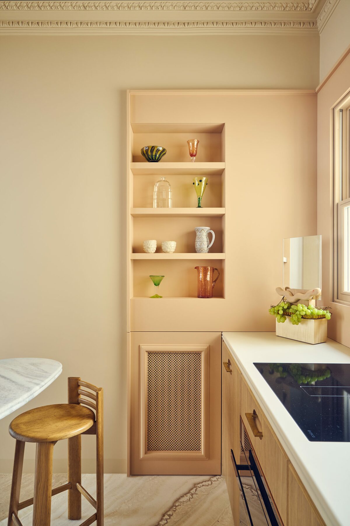 Cuisine ouverte rose pâle et beige. Cuisine haussmannienne avec rangements muraux beiges rosés. Carrelage et parquet. Un projet réalisé par Batiik Studio.