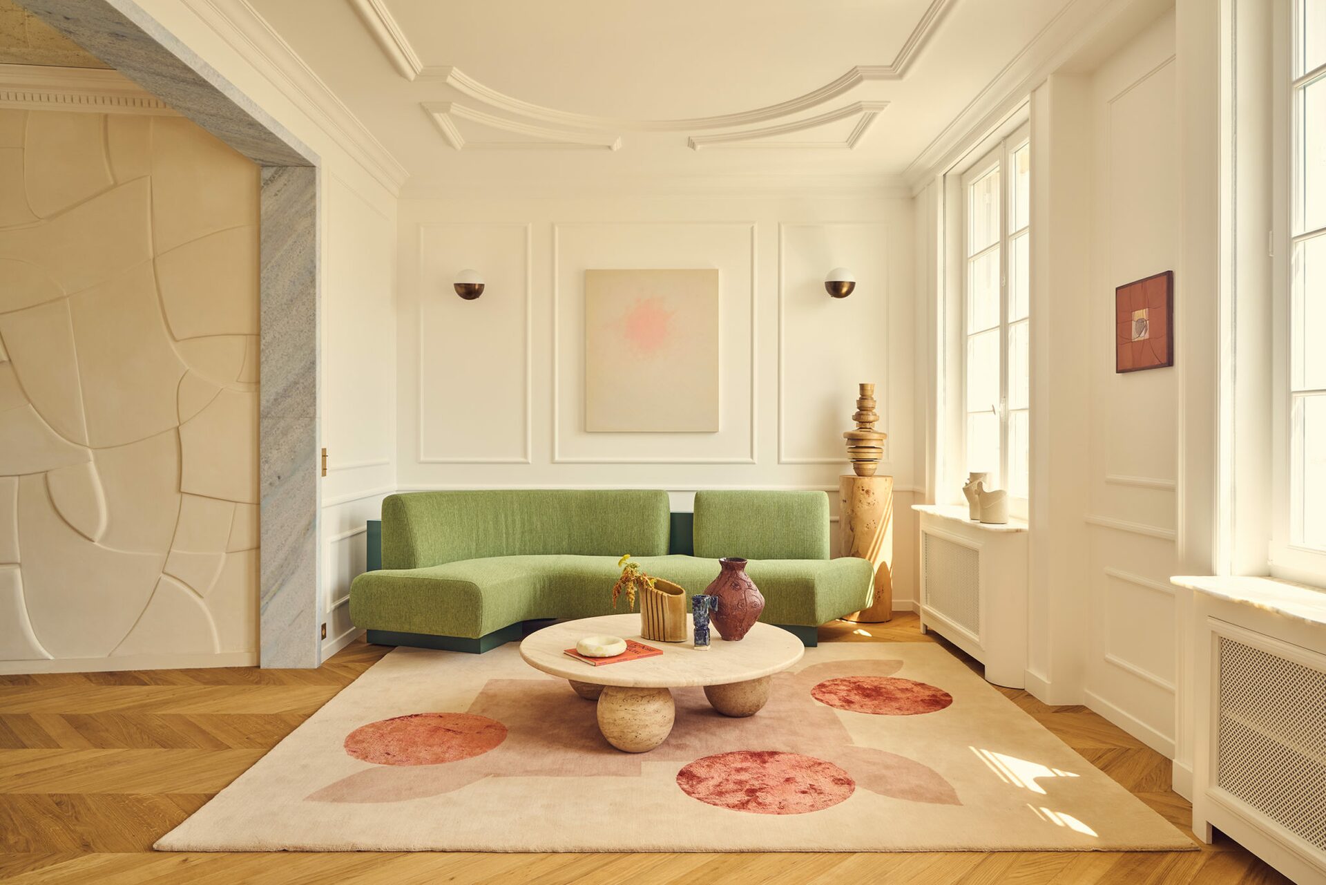 Salon haussmannien avec moulures, tapis géométrique rose, table basse travertin, canapé vert amande avec tissu Pierre Frey. Projet résidentiel Joséphine à Paris signé Batiik Studio.