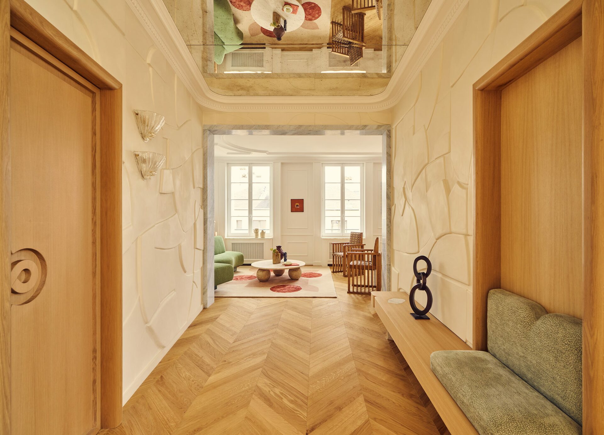 Entrée dans appartement haussmannien avec miroir au plafond, murs blancs en relief, banquette en bois, appliques en verre, tapis graphique avec motifs. Projet résidentiel Joséphine à Paris réalisé par Batiik Studio.