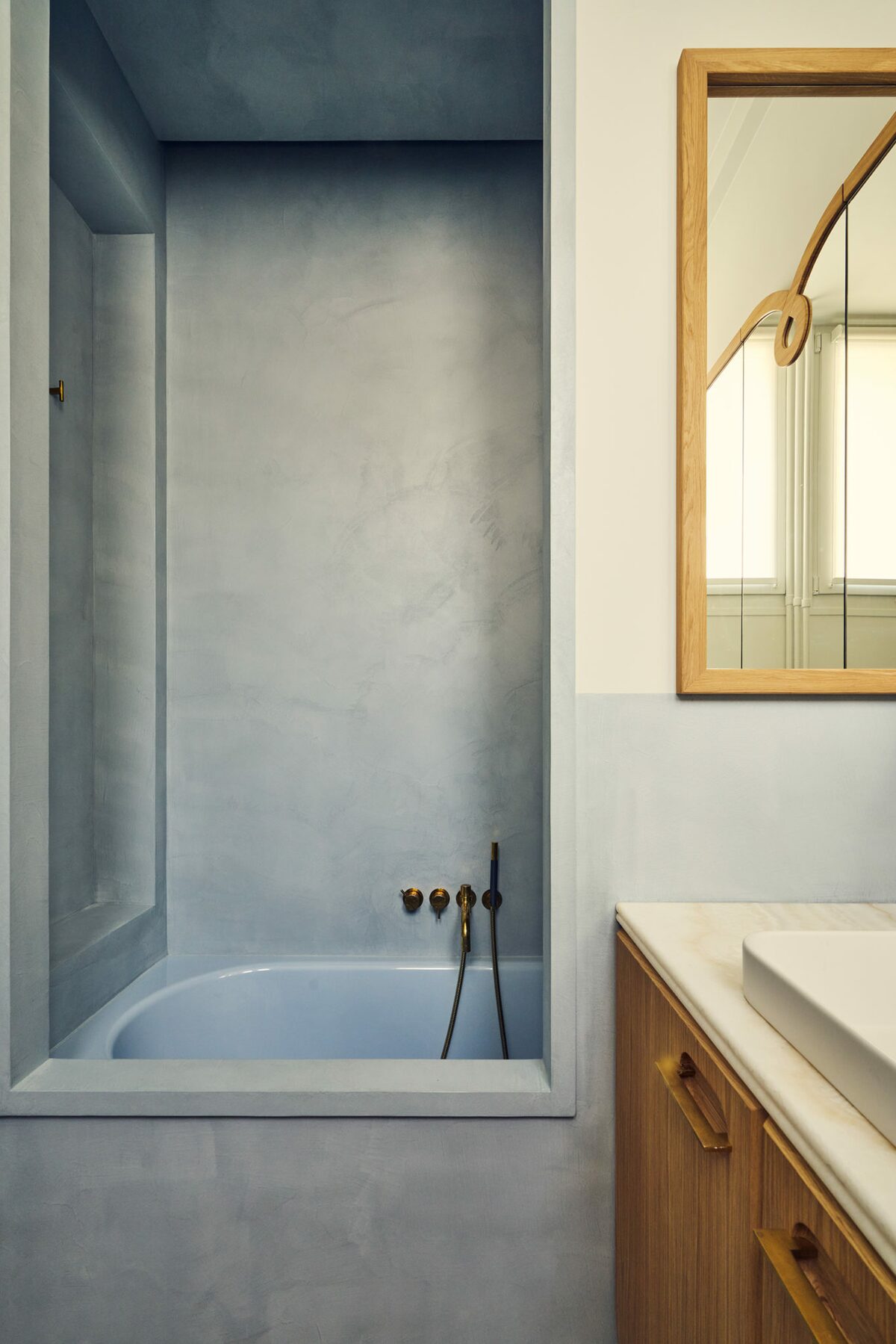 Salle de bain dans appartement haussamnnien chaux bleue avec baignoire dans une alcôve, miroir en bois. Projet Joséphine à Paris signé Batiik Studio.