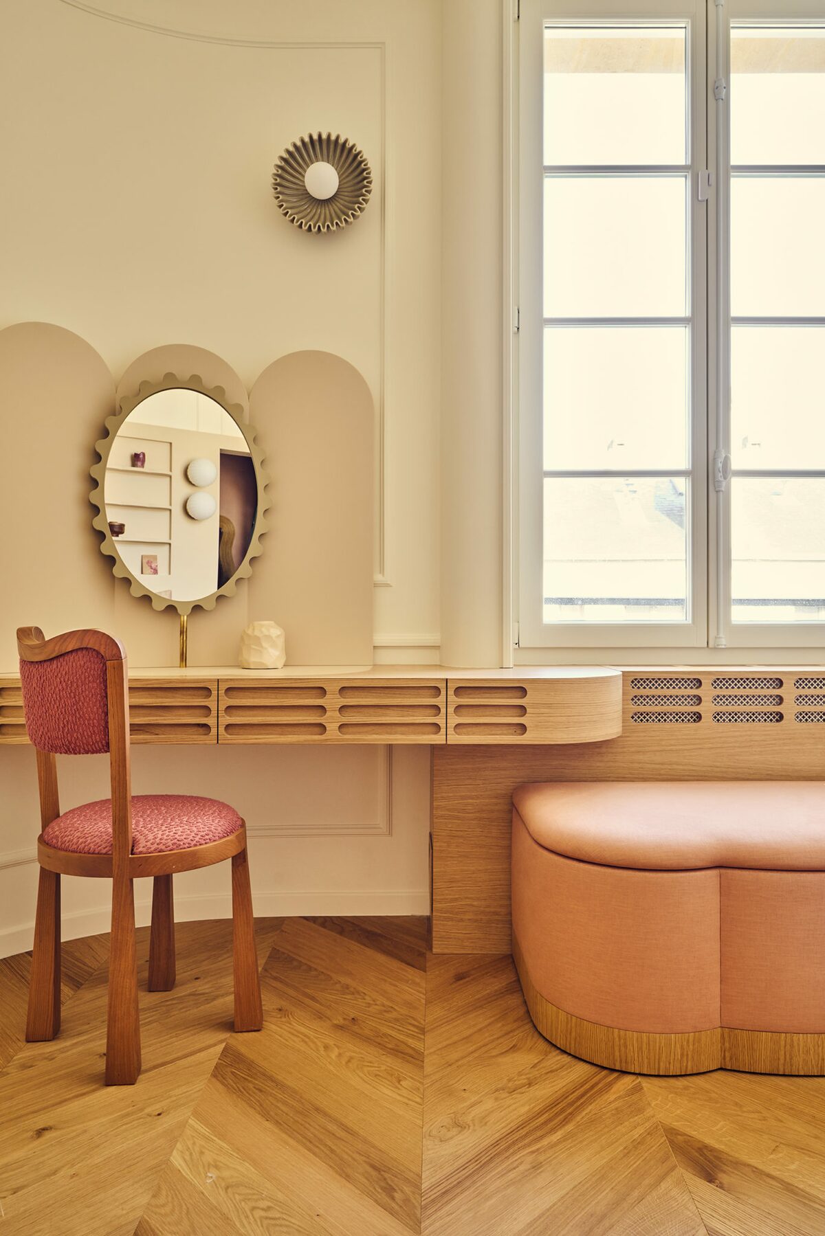 Coiffeuse en bois dans appartement haussmannien avec miroir ovale, banquette en tissu rose. Chaise en bois et tissu rose rouge. Parquet en chevrons dans appartement haussmannien. Projet Joséphine à Paris réalisé par Batiik Studio.