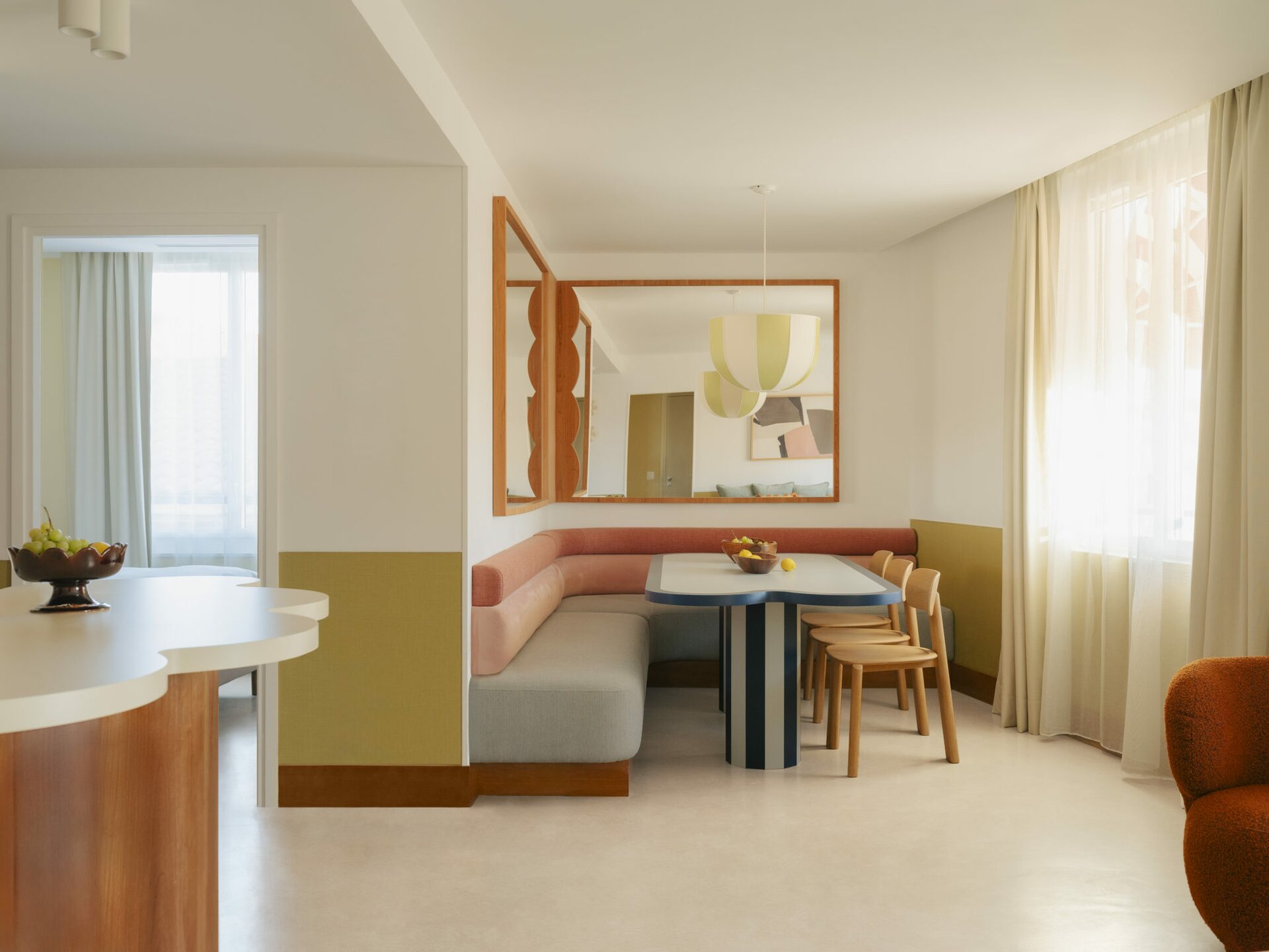 Salle à manger avec banquette en velours rose et table de salle à manger avec pied de table rayé bleu. Miroir en bois d'angle. Style doux et vitaminé, fantaisiste. Projet hôtelier Croisette d'Edgar Suite à Cannes réalisé par Batiik Studio.