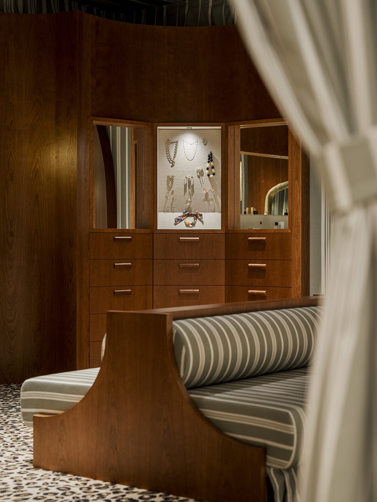 Espace beauté avec rideaux et tapisseries rayées, boiseries aux murs en merisier, banquette rayée, moquette léopard. Un projet réalisé par Batiik Studio pour Balzac Paris pour son adresse lyonnaise.