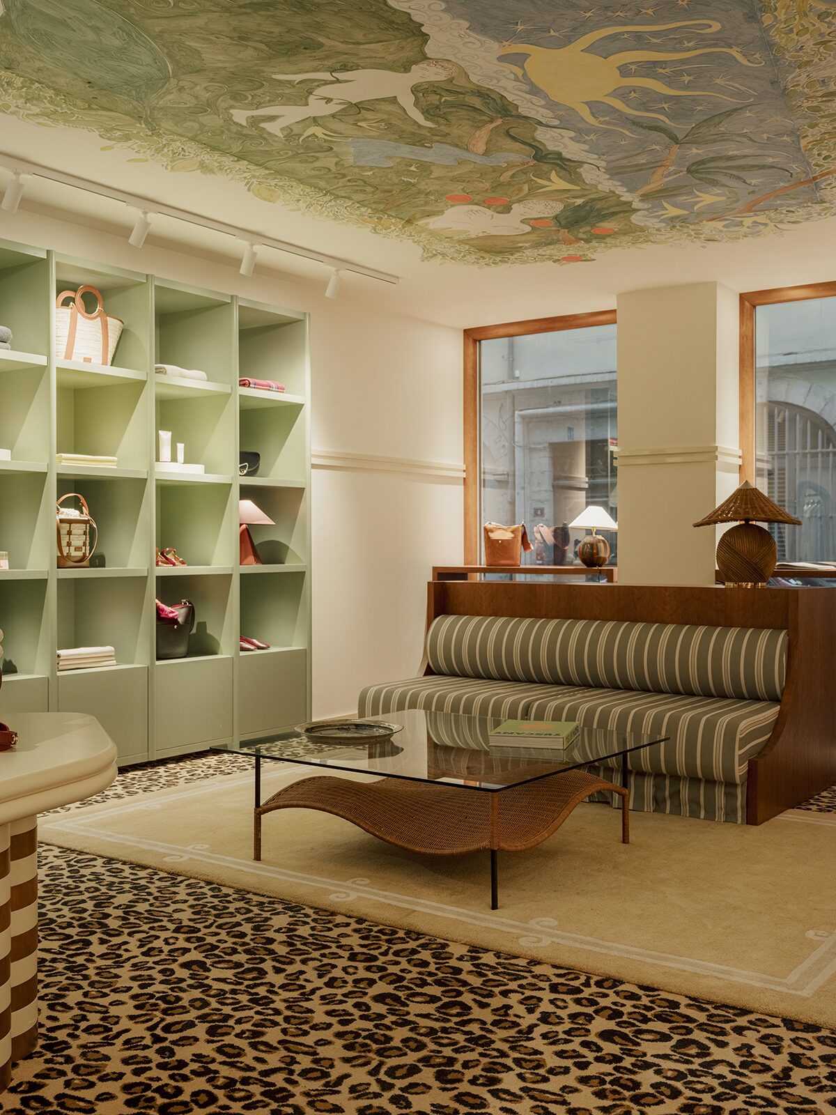 Boutique avec moquette léopard et banquette rayurée. Fresque peinture au plafond et étagère murale vert clair. Un projet réalisé par Batiik Studio pour Balzac Paris dans son adresse lyonnaise.