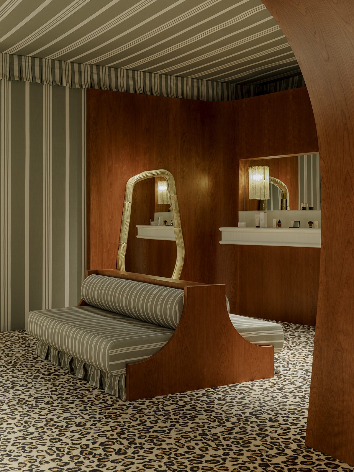 Espace beauté avec rideaux et tapisseries rayées, boiseries aux murs en merisier, banquette rayée, moquette léopard. Un projet réalisé par Batiik Studio pour Balzac Paris.