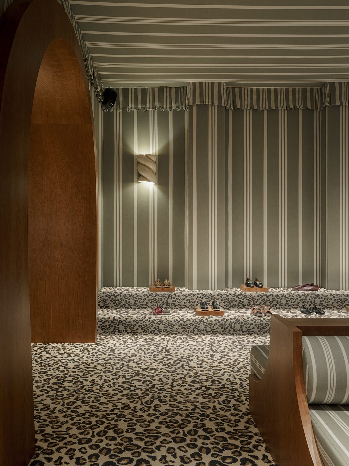 Espace bijou-beauté avec rideaux rayés, moquette léopard, banquette en merisier et rayures. Applique murale en céramique torsadée. Un projet réalisé par Batiik Studio pour Balzac Paris pour son adresse lyonnaise.