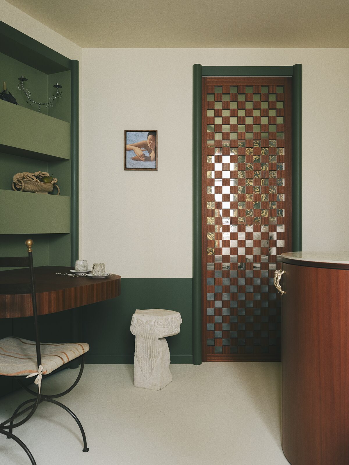 Salon vert avec tablette en bois, chaise en fer forgé, porte à damier en bois et verre donnant sur la chambre à papier-peint. Projet Chevalier à Paris réalisé par Batiik Studio.