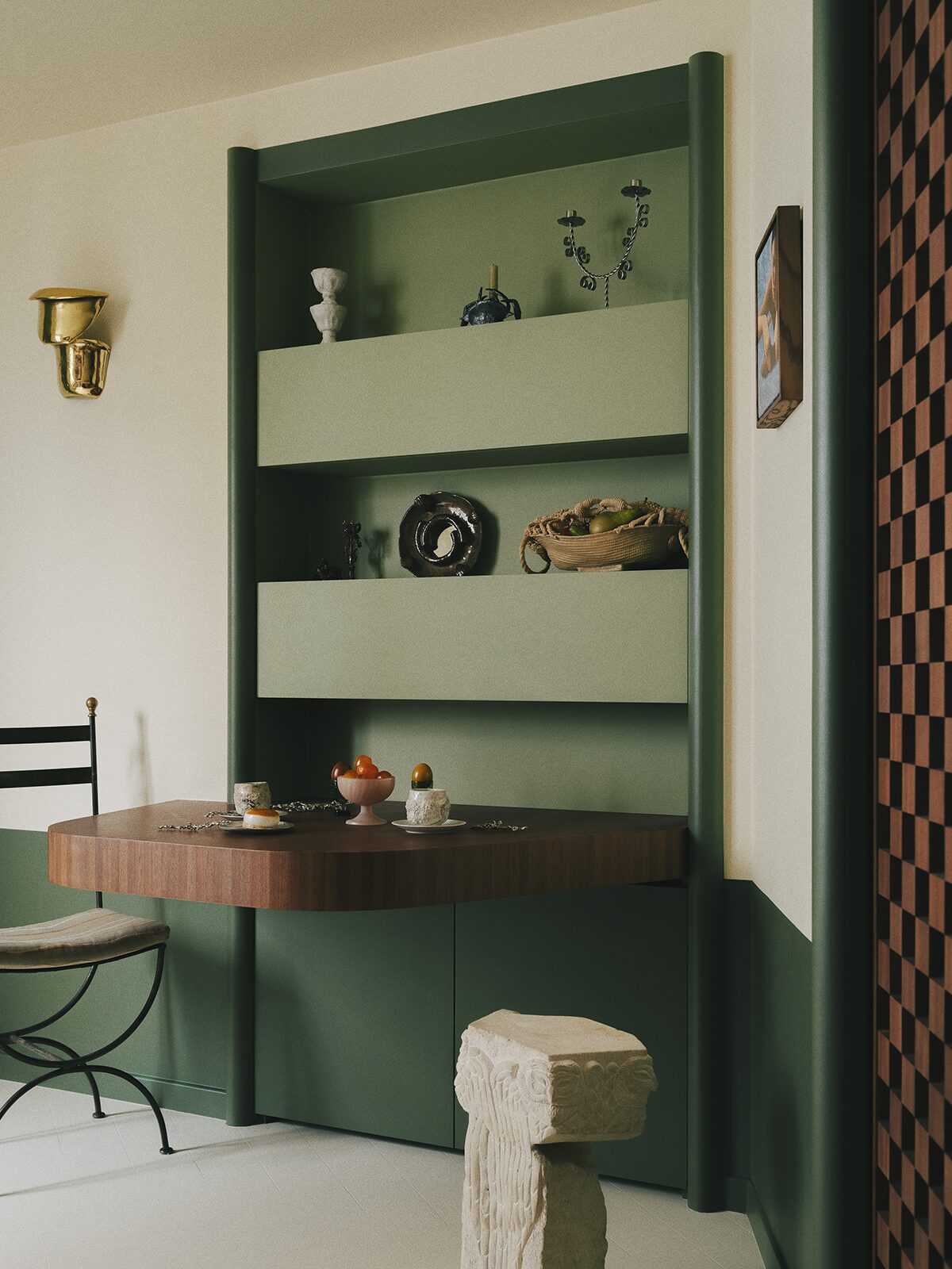Salon vert avec ilôt central en bois, niche verte et applique en laiton, frise en bois murale, chaise en fer forgé. Projet Chevalier réalisé par Batiik Studio.