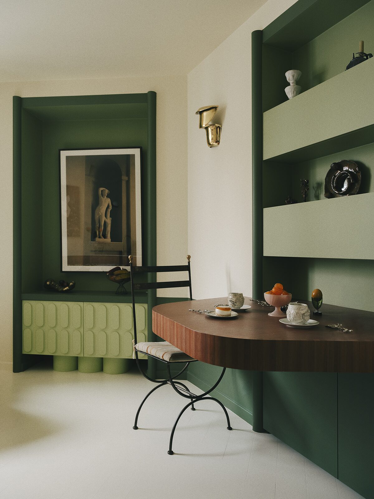 Salon vert avec ilôt central en bois, niche verte et applique en laiton, frise en bois murale, chaise en fer forgé. Projet Chevalier réalisé par Batiik Studio.