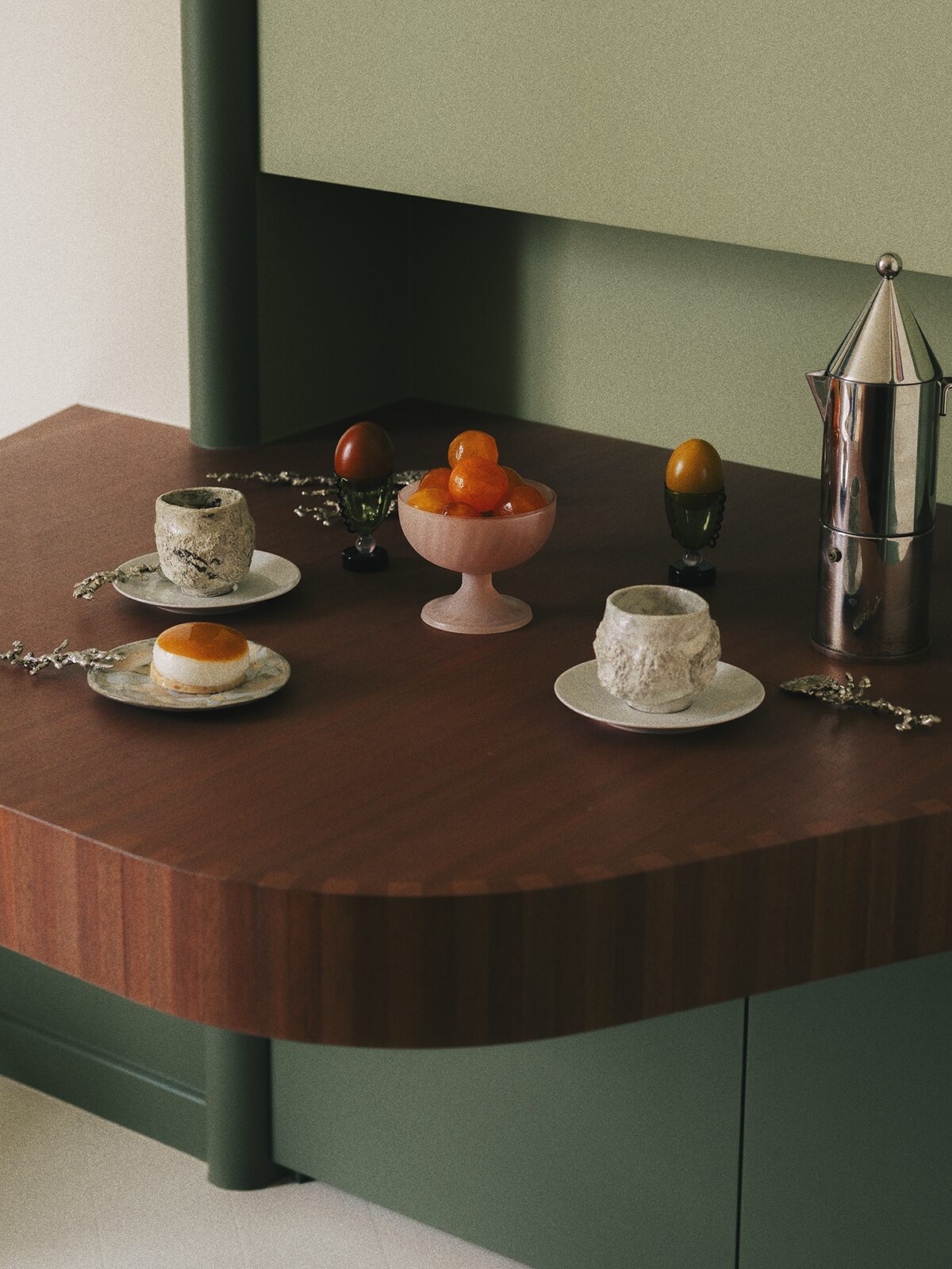 Tablette en bois et set up design avec thé et café. Mur bibliothèque verte, cafetière Alessi, tasses en céramique. Coquetier Sophie Lou Jacobsen. Projet Chevalier réalisé à Paris par Batiik Studio.