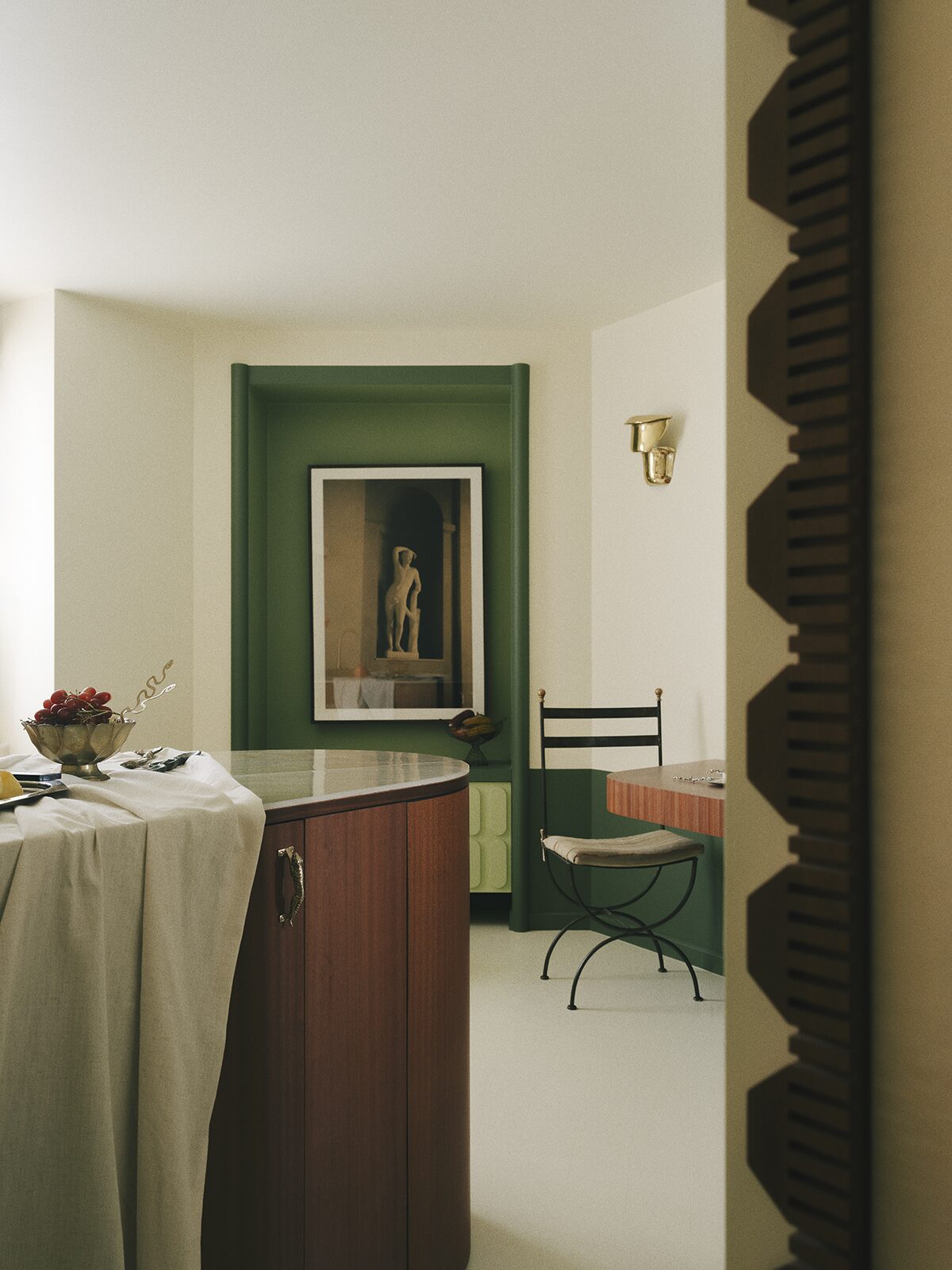Salon vert avec ilôt central en bois, niche verte et applique en laiton, frise en bois murale, chaise en fer forgé. Projet Chevalier réalisé à Paris par Batiik Studio.